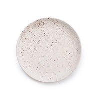 A round ceramic plate with a speckled beige and brown glaze, photographed from directly above on a clean white background.