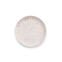 A round ceramic plate with a speckled beige and brown glaze, photographed from directly above on a solid white background.