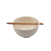 A speckled cream-colored ceramic bowl with a small wooden chopstick resting across the top, set against a plain white background.