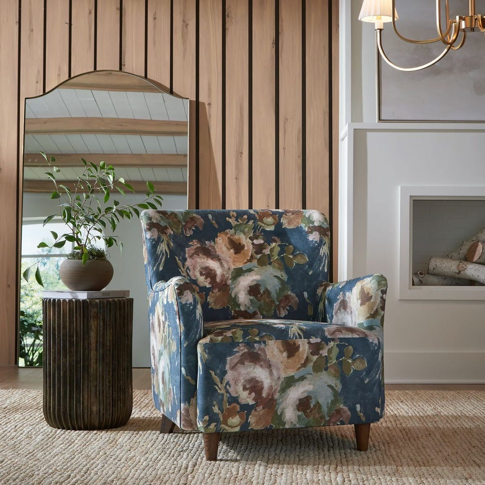 Floral patterned armchair in a room with wooden walls and a mirror.