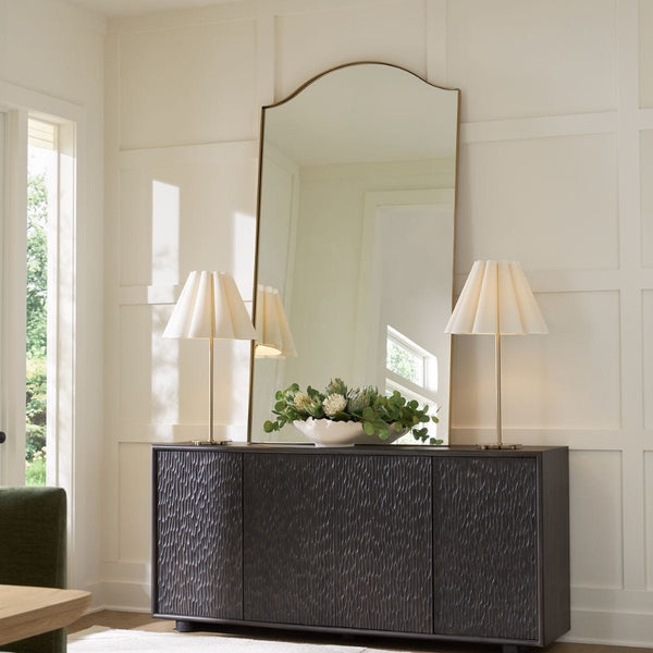 Dark wooden sideboard with a large mirror and lamps in a room with white walls and a window.