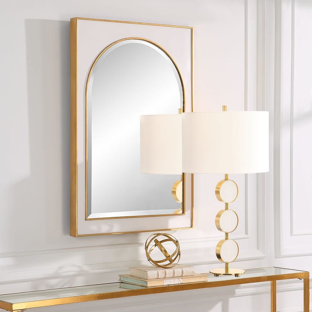 Decorative mirror with gold frame and lamp on a console table against a white wall.