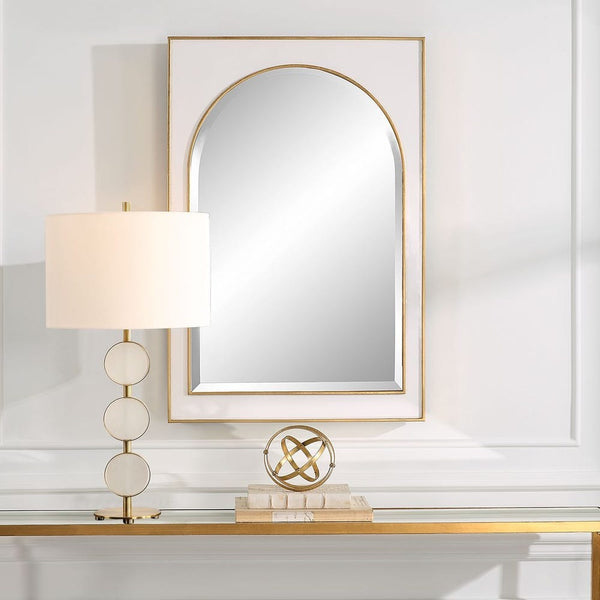 Decorative mirror with gold frame on a wall above a console table with a lamp and decorative object.