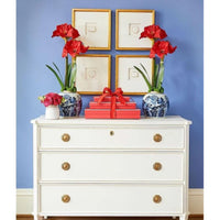 A white dresser with red flowers in vases and wrapped gifts is set against a blue wall featuring Shadow Catchers Art's Framed Intaglio Art in Gold - Style 2.