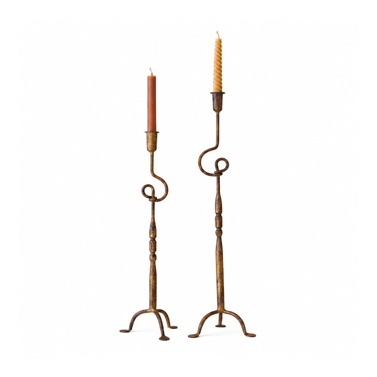 Two tall metal candlestick holders with scrolled arms and tripod bases, each holding a taper candle.