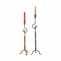 Two tall metal candlestick holders with scrolled arms and tripod bases, each holding a taper candle.