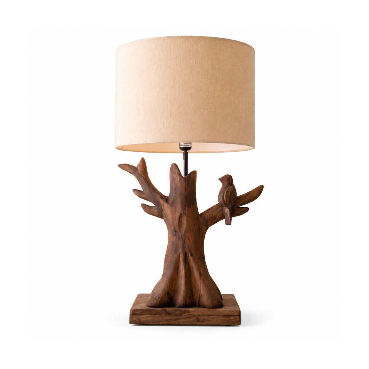 A rustic wooden table lamp shaped like a tree trunk with a small bird perched on one branch, featuring a beige fabric drum shade.