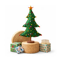 Green felt christmas tree with colored pom pom balls with a wooden base standing on a rattan riser and wrapped presents on a white background.