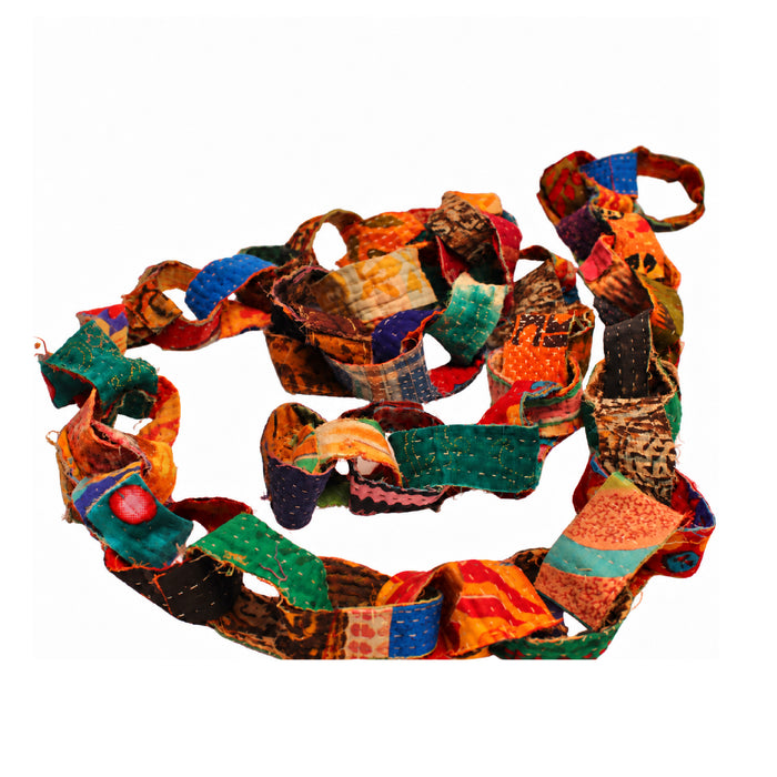 A handmade patchwork fabric garland made of colorful stitched fabric strips in orange, green, blue, brown, and red, arranged in a loose spiral on a plain white background.