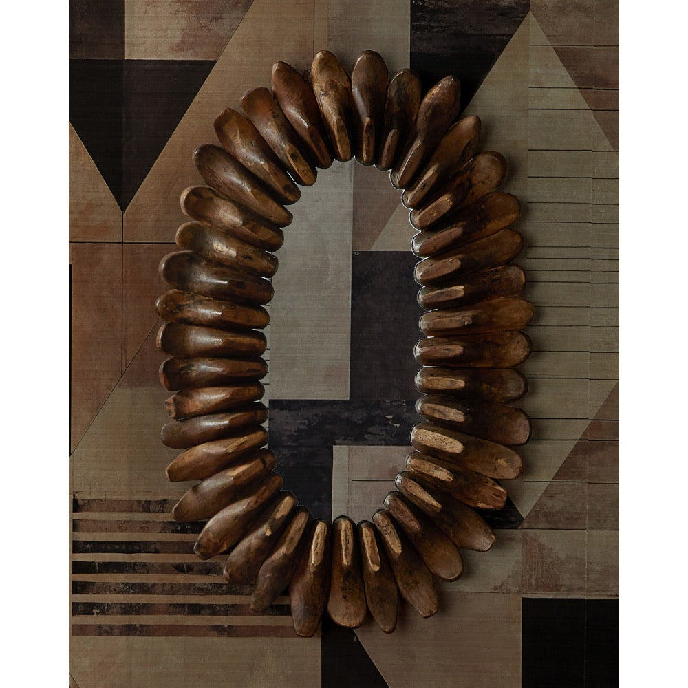 An oval wall mirror with a decorative frame made of many curved wooden pieces arranged in a sunburst pattern, mounted on a geometric patterned wall.