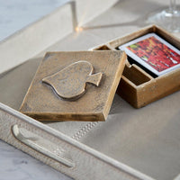 A square decorative box with a raised spade symbol on the lid, shown open with a card or small item inside, placed on a light beige tray.