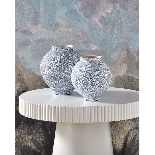 Two patterned vases on a white table against a textured wall.