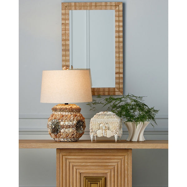 Decorative lamp with seashell details on a wooden table against a gray wall with a mirror.