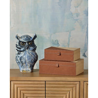Blue owl figurine and two brown boxes on a wooden surface with a watercolor wall background