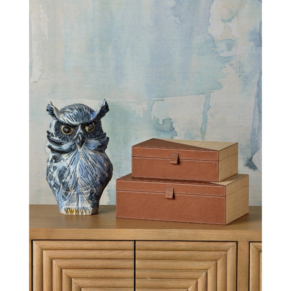 Blue owl figurine and two brown boxes on a wooden surface with a watercolor wall background