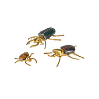 Three beetle-shaped decorative figurines in polished gold-tone metal with colored beetle wings, shown on a plain white background.