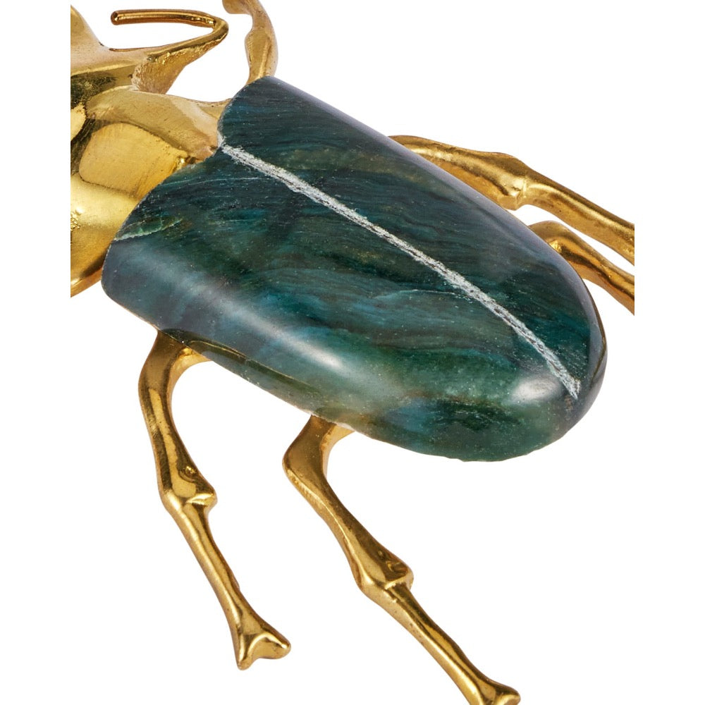 A close-up of a beetle sculpture with a polished gold-tone metal body and a dark green to blue-green stone elytra on a white background.