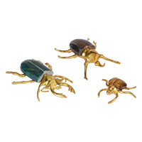 Three beetle-shaped decorative figures in polished gold-tone metal with natural brown beetle wings, displayed on a clean white background.