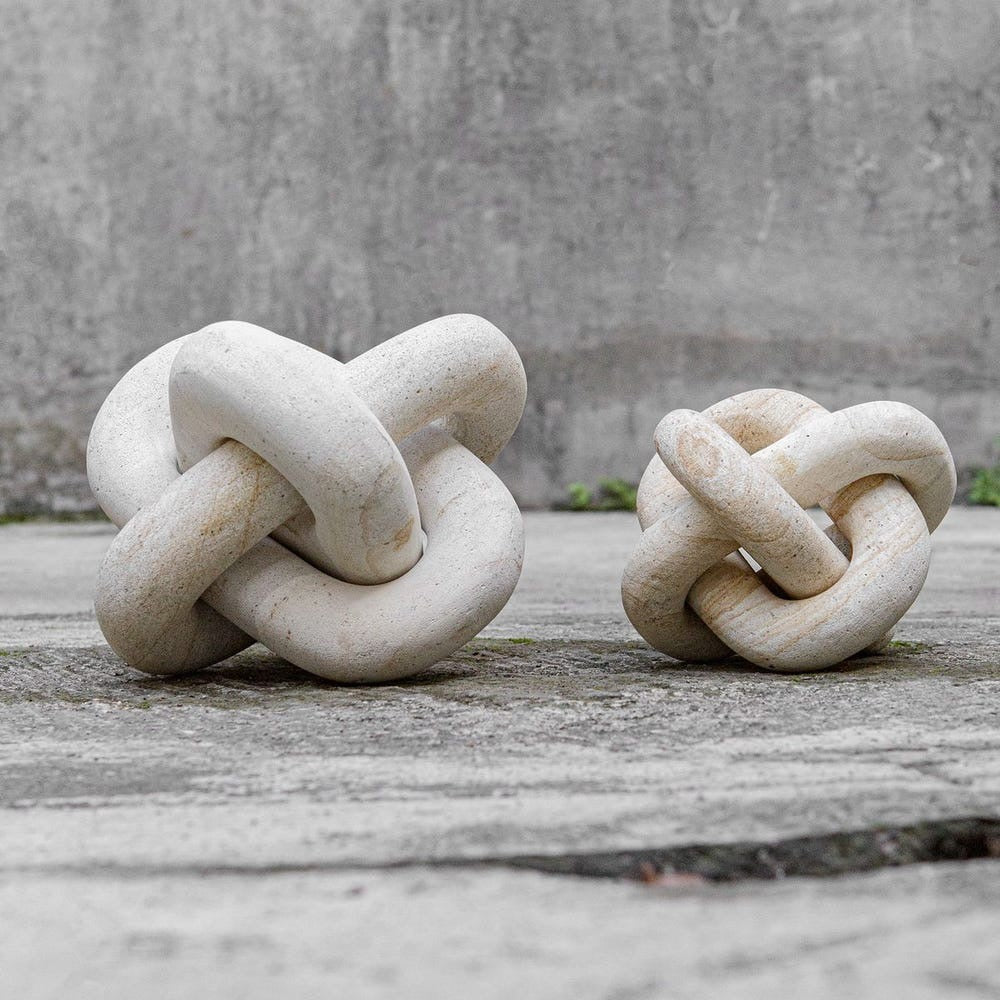 Two stone knot sculptures on a wooden surface with a concrete wall background