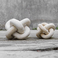 Two stone knot sculptures on a wooden surface with a concrete wall background