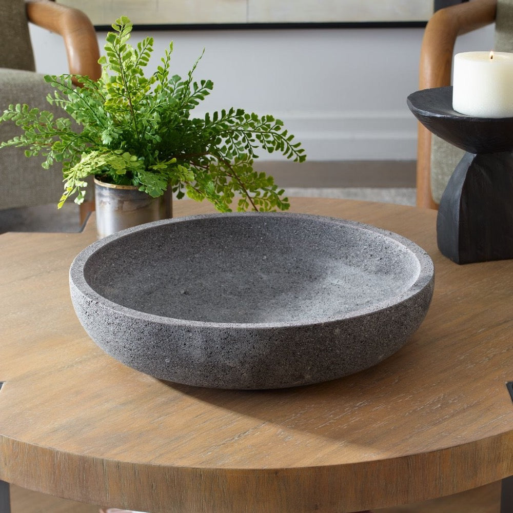 Dark grey bowl on a wooden table with a plant and candle in the background