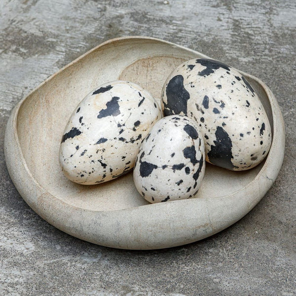 Three speckled eggs in a ceramic dish on a concrete surface