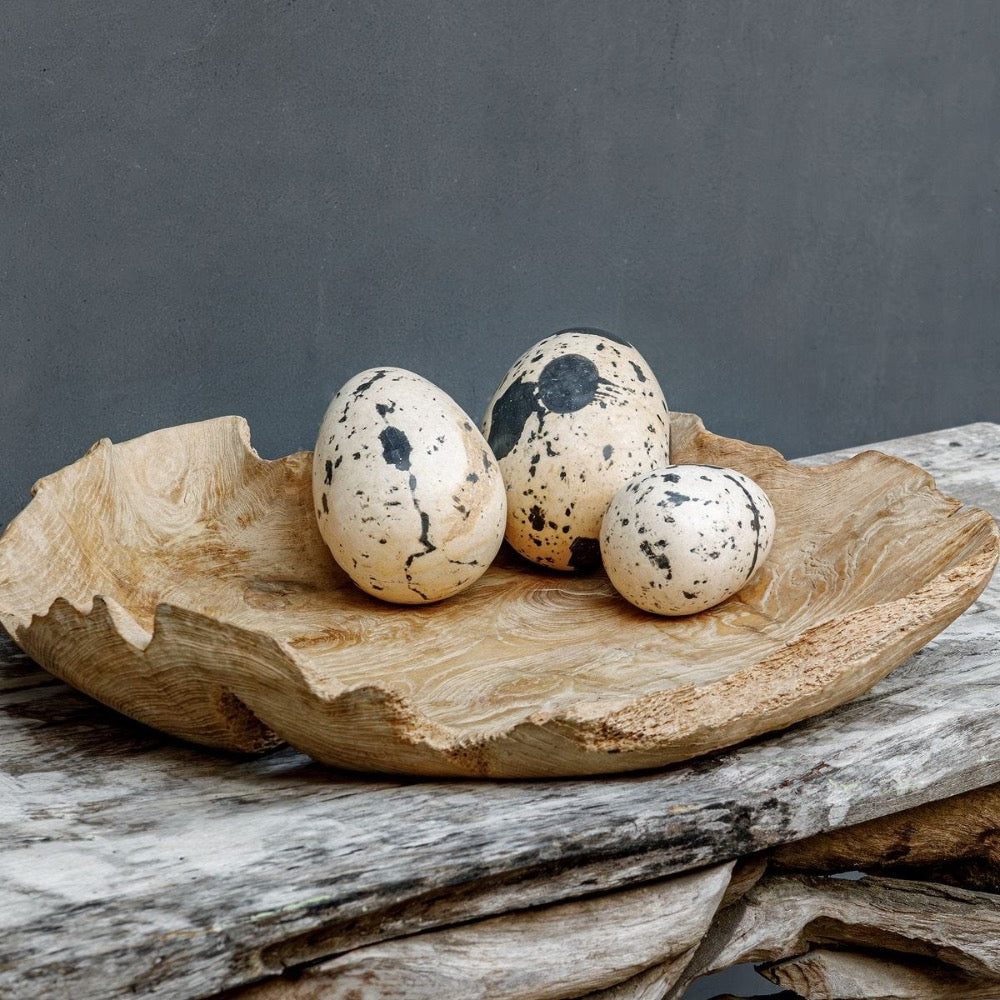 Three speckled eggs in a wooden bowl on a rustic background