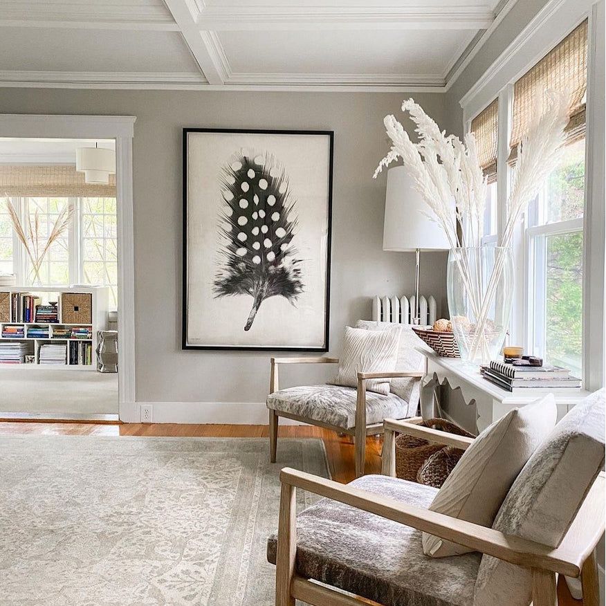 Bright, cozy living room with neutral tones featuring Barloga Studios' Feather Study 1 Photography Art, comfortable armchairs, and a sunlit window nook. The Feather Study 1 art adds a natural touch while offering versatile hanging options.