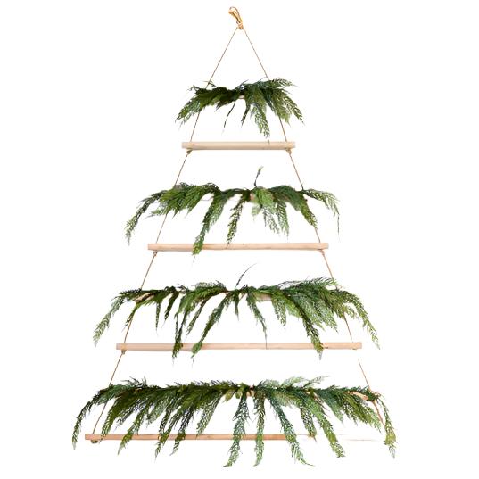 The Tall Hanging Wood + Jute Tree Display by Sugarboo & Co. is a wall-mounted wooden frame measuring 6 feet, adorned with pine branches on each tier and fairy lights for a festive holiday touch.