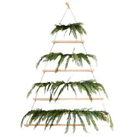 The Tall Hanging Wood + Jute Tree Display by Sugarboo & Co. is a wall-mounted wooden frame measuring 6 feet, adorned with pine branches on each tier and fairy lights for a festive holiday touch.