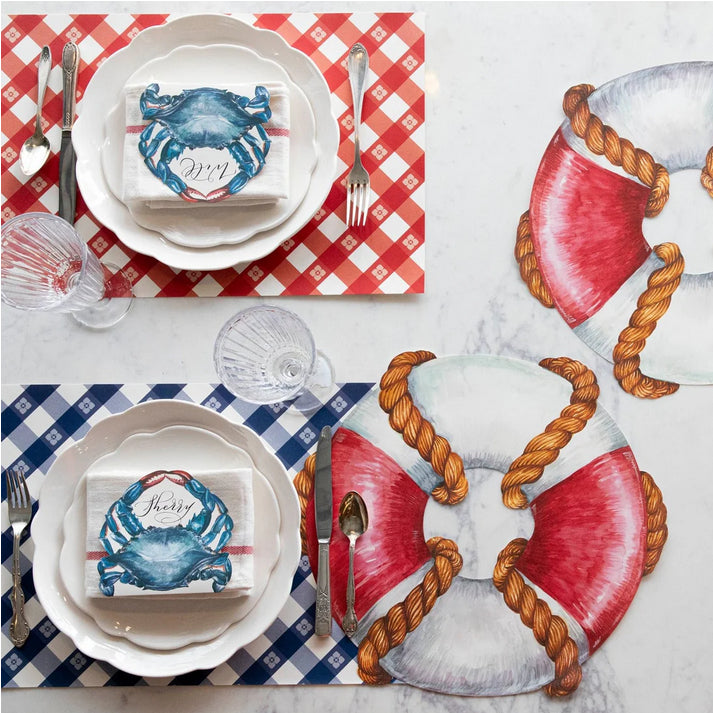 Hester & Cook's nautical-themed table setting showcases life rings and crab motifs on the Picnic Check Red + Blue Paper Placemats Pad, beautifully printed with soy-based ink, complemented by checkered plates and napkins.