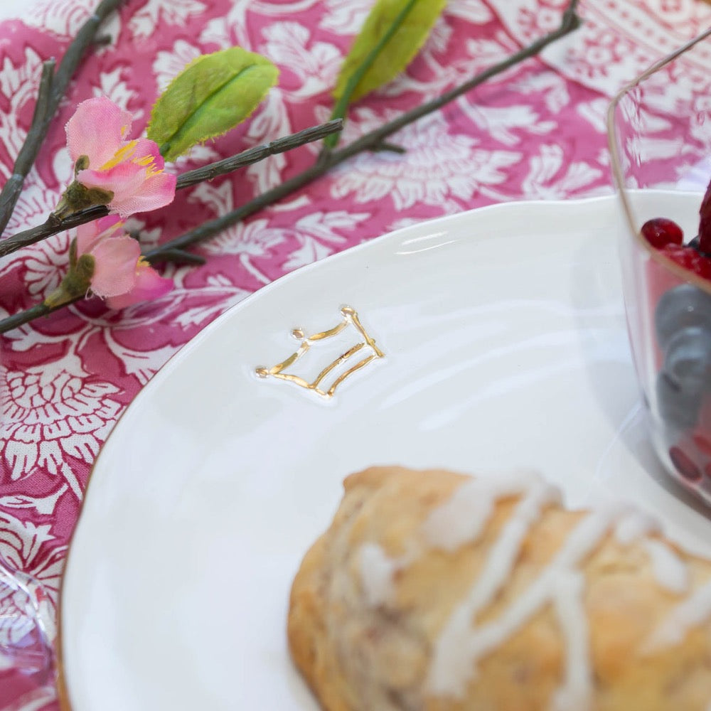 Pastry on a plate with a decorative gold crown, pink flowers, and a floral tablecloth.