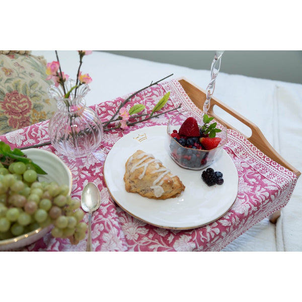 Table setting with a plate of scone, berries, and grapes on a floral tablecloth.