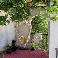 The Under The Bough Hand Loomed Hanging Hammock Chair features a yellow pillow and pink rug, perfect for your patio.
