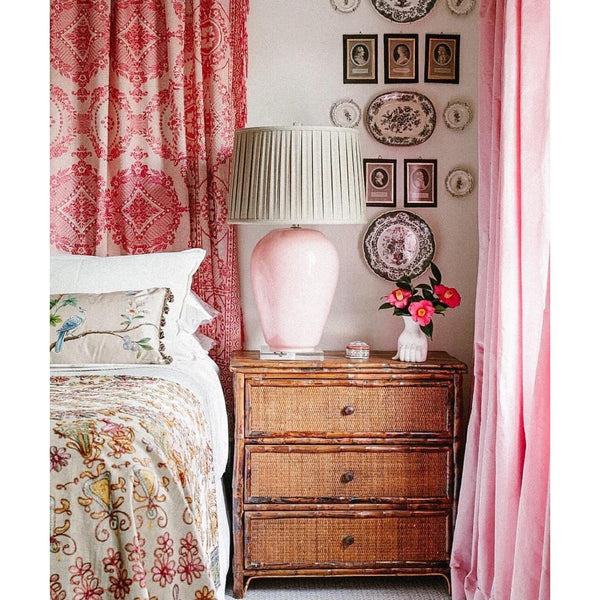 Bedroom corner with Kenian Tortoise Shell Bamboo Bedside Chest, pink lamp, plate wall decor, pink curtains, and bedding.