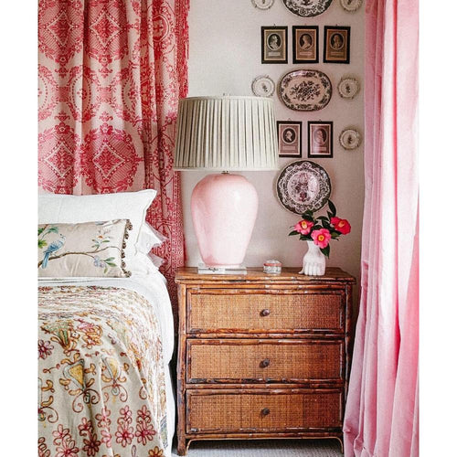 Bedroom corner with Kenian Tortoise Shell Bamboo Bedside Chest, pink lamp, plate wall decor, pink curtains, and bedding.