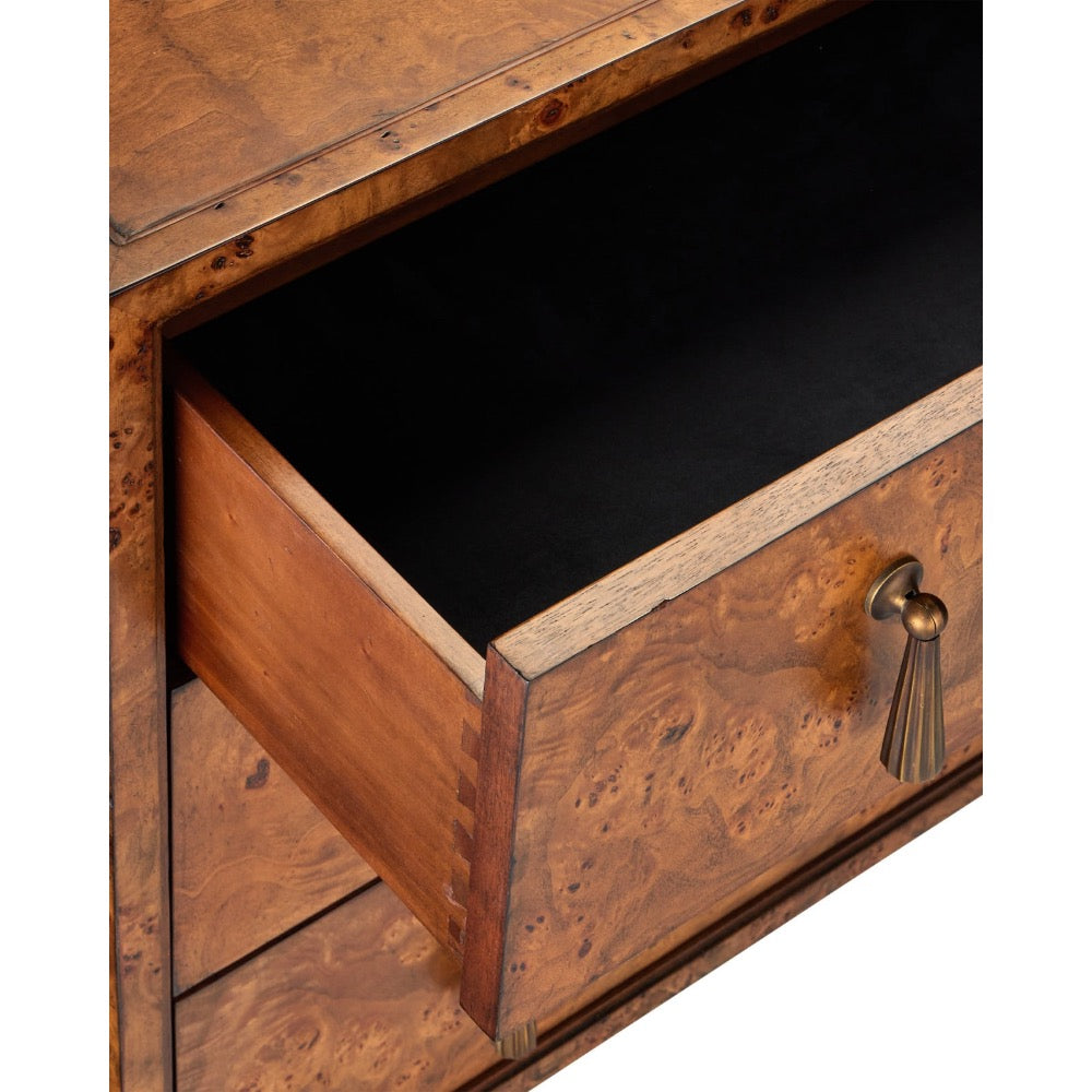 Close-up of a wooden drawer with a burl wood grain finish, partially open to reveal a black interior, featuring a brass pull handle with a tassel detail.
