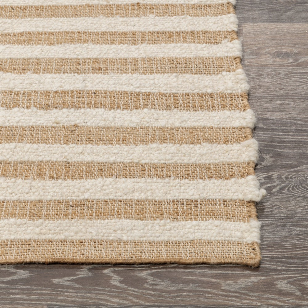 A close-up of a woven rug with horizontal stripes in natural tan and off-white, laid on a gray wood floor.