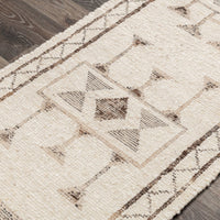 A close-up of a textured area rug with a geometric tribal pattern in beige and brown, laid out on a dark wood floor.