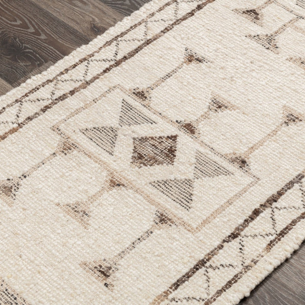 A close-up of a textured area rug with a geometric tribal pattern in beige and brown, laid out on a dark wood floor.