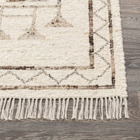 Textured area rug with geometric pattern and white fringe on a wooden floor.