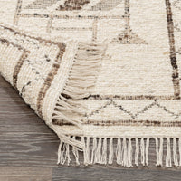 Close-up of a textured rug with geometric pattern and fringes on a wooden floor.