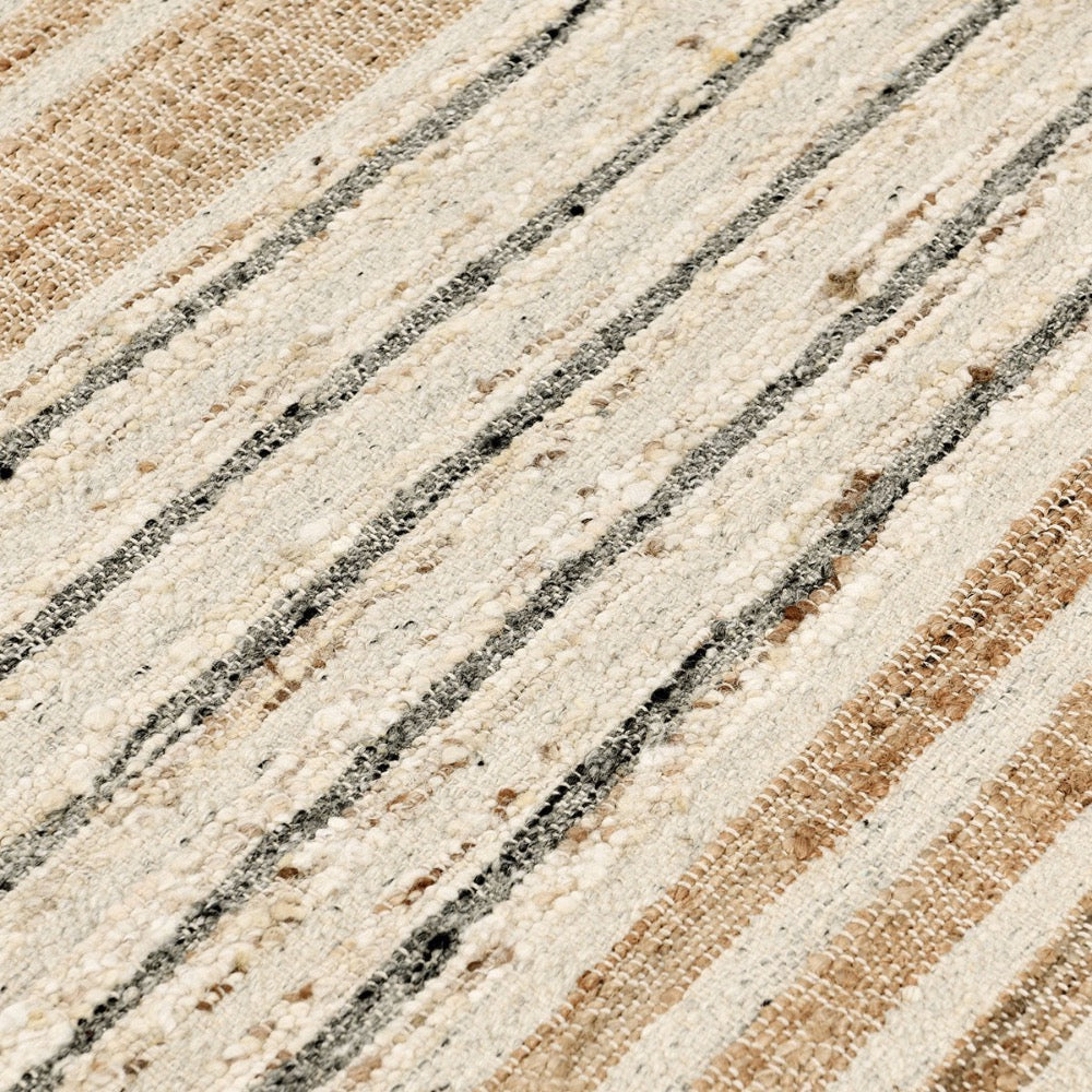 A close-up of a woven rug or textile with diagonal stripes in cream, beige, and dark charcoal gray, showing the detailed texture of the fibers.