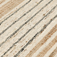 A close-up of a woven rug or textile with diagonal stripes in cream, beige, and dark charcoal gray, showing the detailed texture of the fibers.