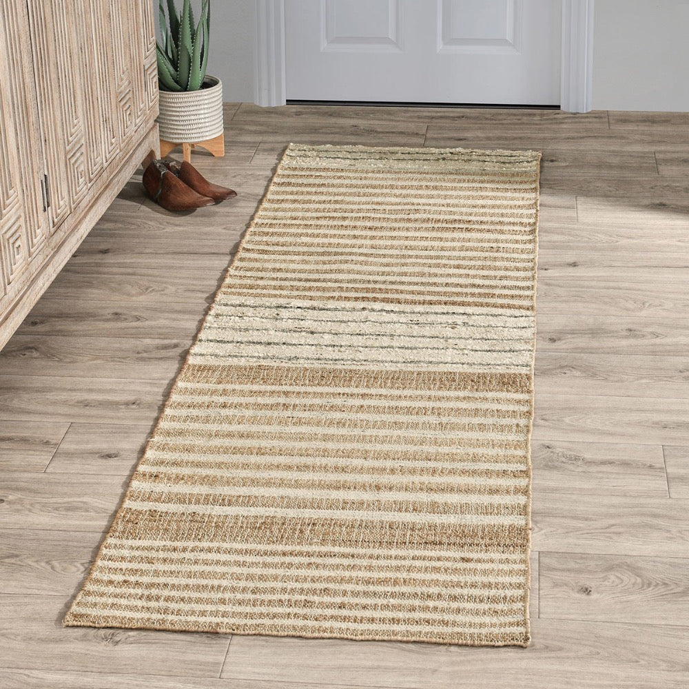 Beige runner rug on a wooden floor with a plant and shoes in the background