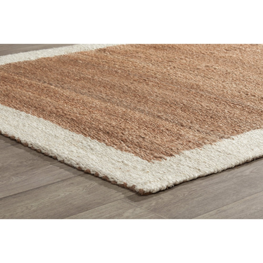 A close-up of a textured area rug with a warm brown center and an off-white border, shown on a gray wood-look floor.