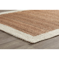 A close-up of a textured area rug with a warm brown center and an off-white border, shown on a gray wood-look floor.
