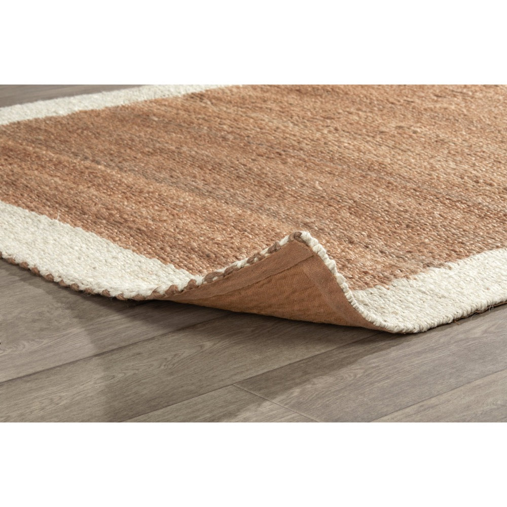 A close-up of a textured area rug with a warm brown center and cream-colored borders, shown partially folded over on a gray wood-look floor.
