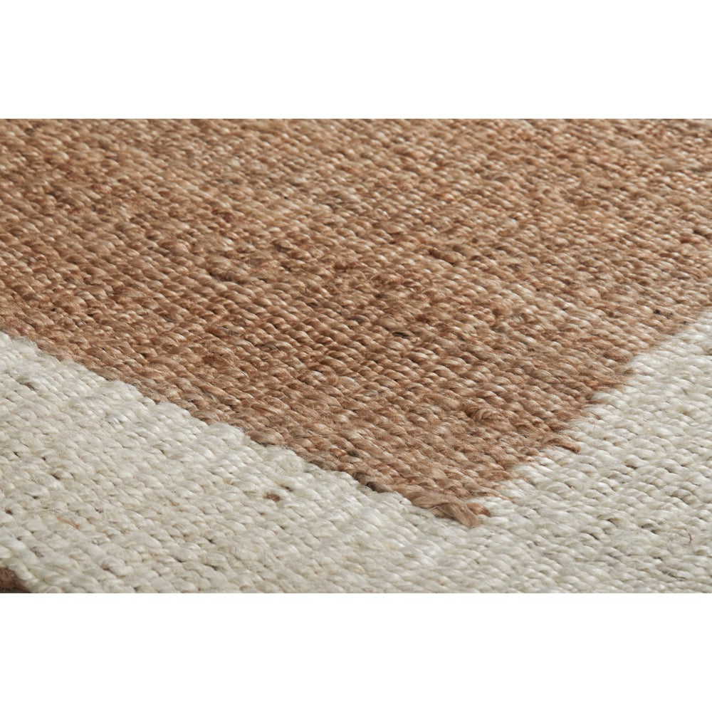 Close-up of a woven rug showing a textured natural tan section meeting an off-white section, with visible weave detail and no visible branding.