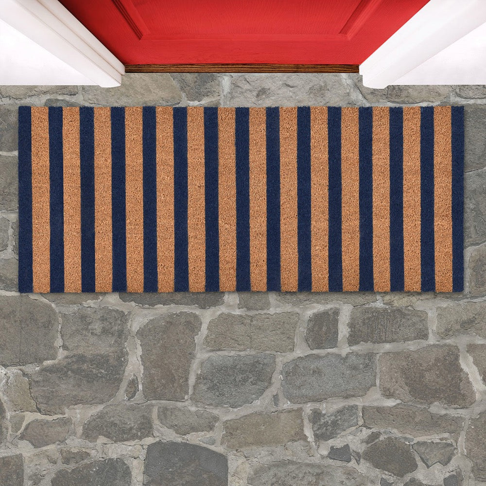 Striped doormat with blue and brown stripes on a stone floor in front of a red door.
